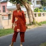 Full shot of a model standing on an outdoor road in a premium terracotta cotton co-ord set, featuring a structured dual-pocket longline blazer top and pleated hem crop trousers.
