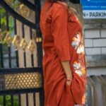 Side profile shot of a model with her hand in her pocket, highlighting the clean stitching, longline cut of the rust orange blazer top, and the placement of the hand-painted flowers