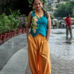 Full-length portrait of a woman standing outdoors in a modern teal and yellow hand-painted co-ord set with hands in her pockets
