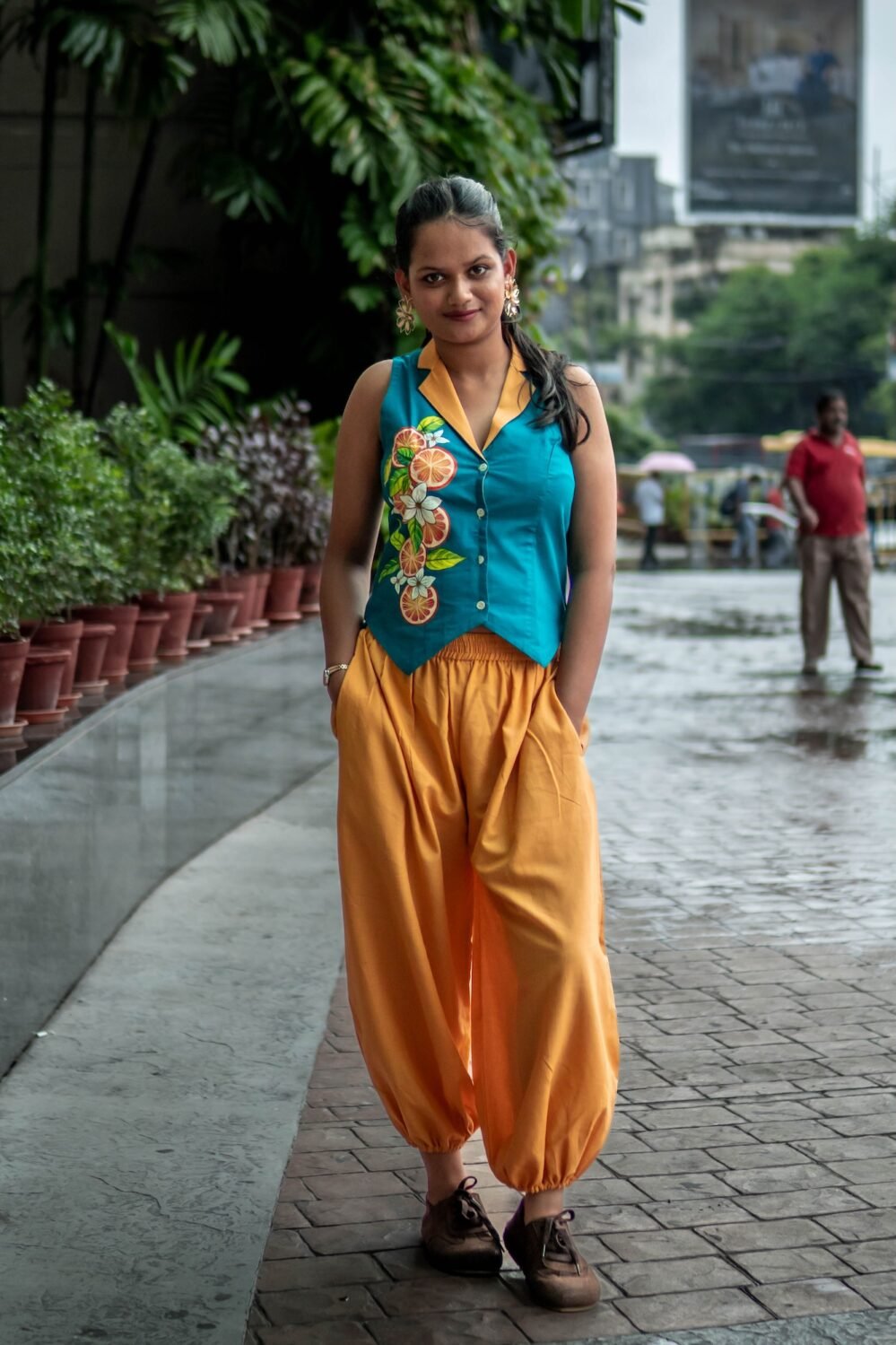 Full-length portrait of a woman standing outdoors in a modern teal and yellow hand-painted co-ord set with hands in her pockets