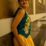 Side angle shot of a woman looking over her shoulder indoors, highlighting the hand-painted orange fruit pattern on her teal waistcoat