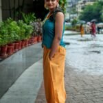 Side angle shot of a woman looking over her shoulder indoors, highlighting the hand-painted orange fruit pattern on her teal waistcoat