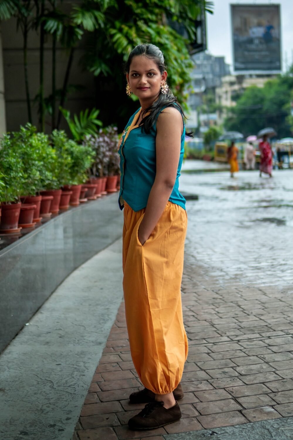 Side angle shot of a woman looking over her shoulder indoors, highlighting the hand-painted orange fruit pattern on her teal waistcoat