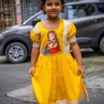 Front view of a child standing outdoors in the yellow handpainted Durga Dulali cotton frock featuring brocade accents.