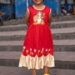 Full front view of girl smiling in red handpainted Durga Rani frock with lotus motifs by Aankibukis Couture.