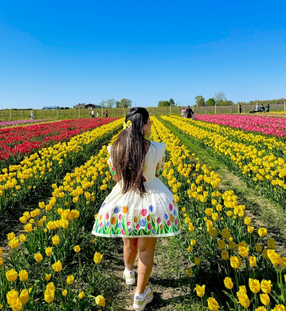 Back view of a woman walking through a yellow tulip field wearing the off-white handpainted tulip short dress by Aankibukis Couture