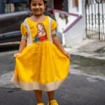 Full-length view of a little girl wearing the handpainted Durga Dulali yellow cotton frock.