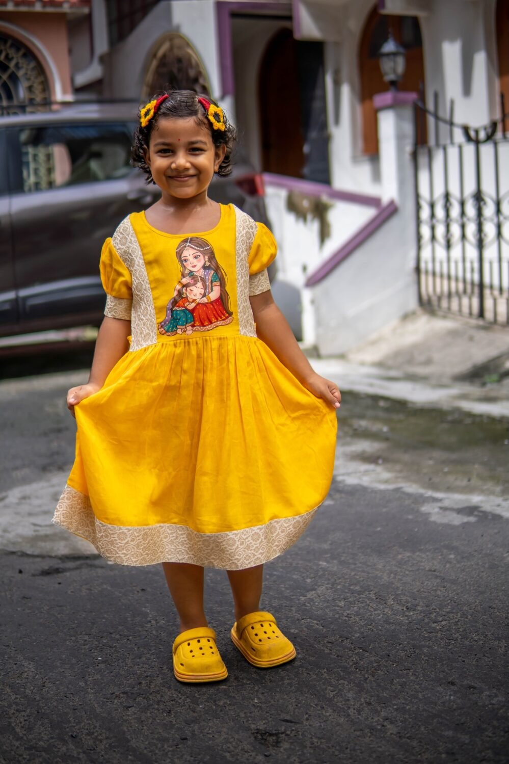 Full-length view of a little girl wearing the handpainted Durga Dulali yellow cotton frock.