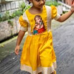 Little girl walking outside in a bright yellow handpainted Durga Dulali cotton frock by Aankibukis Couture.