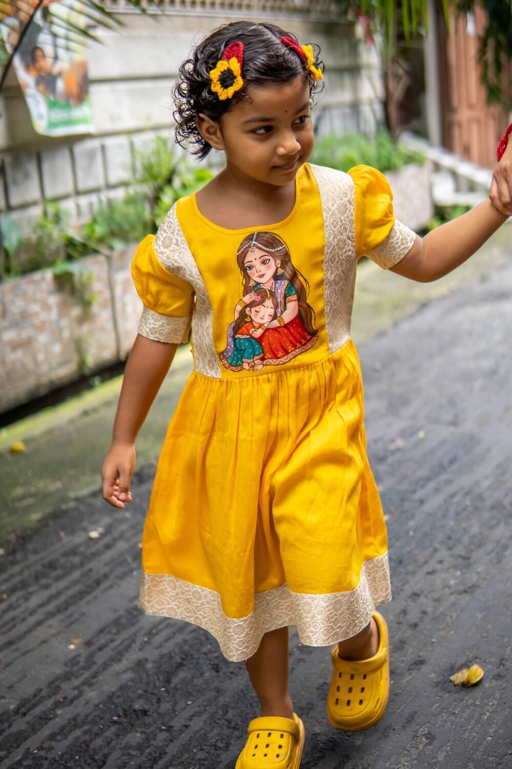 Little girl walking outside in a bright yellow handpainted Durga Dulali cotton frock by Aankibukis Couture.