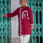 Full-length view of a boy posing in the Agamani maroon hand painted dhoti kurta set with lotus and Durga artwork.