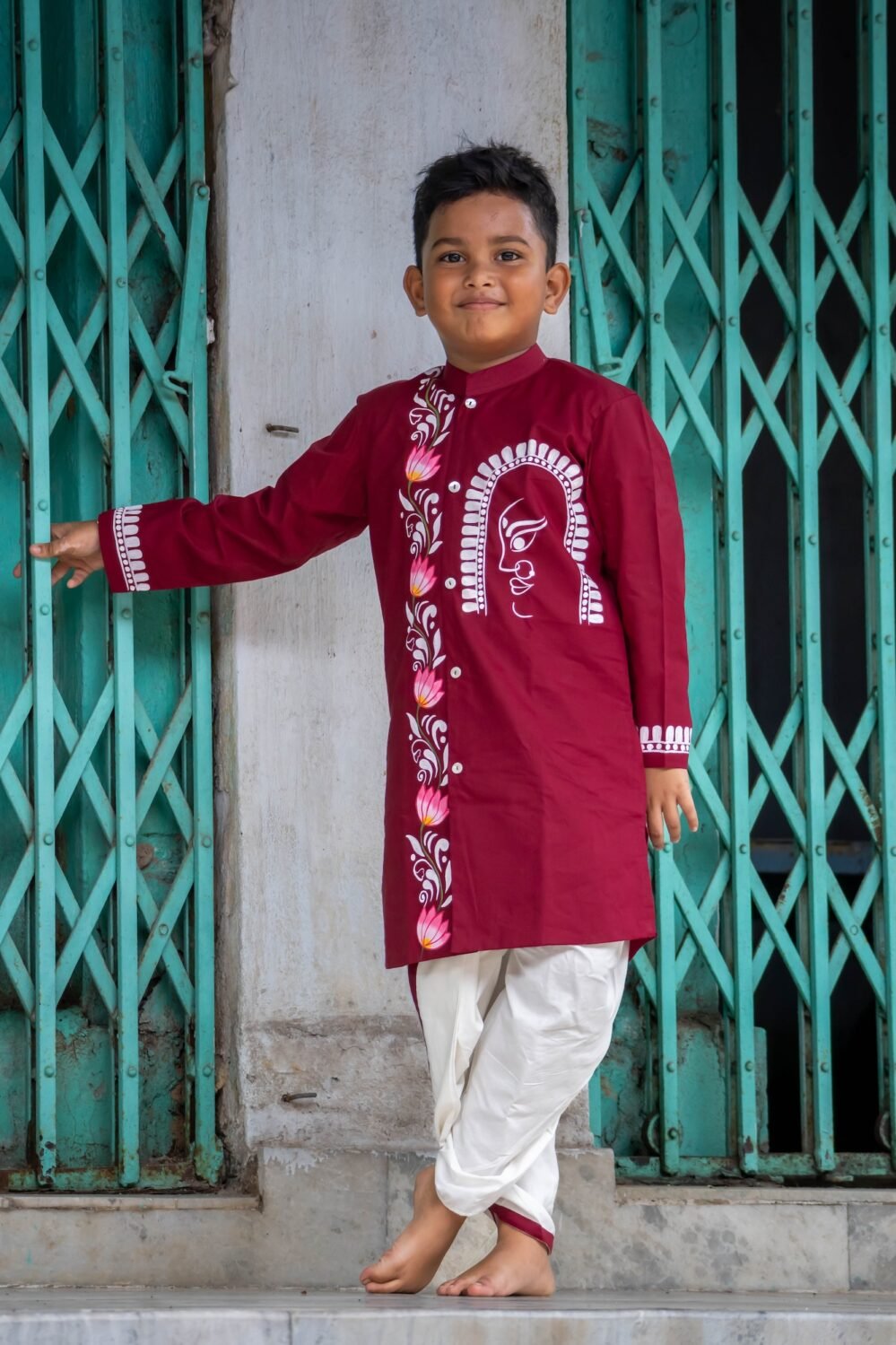 Full-length view of a boy posing in the Agamani maroon hand painted dhoti kurta set with lotus and Durga artwork.