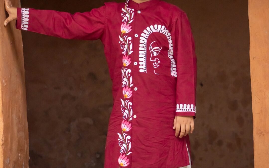 Boy standing in a traditional doorway wearing a maroon hand painted Durga motif kurta with an off-white dhoti.