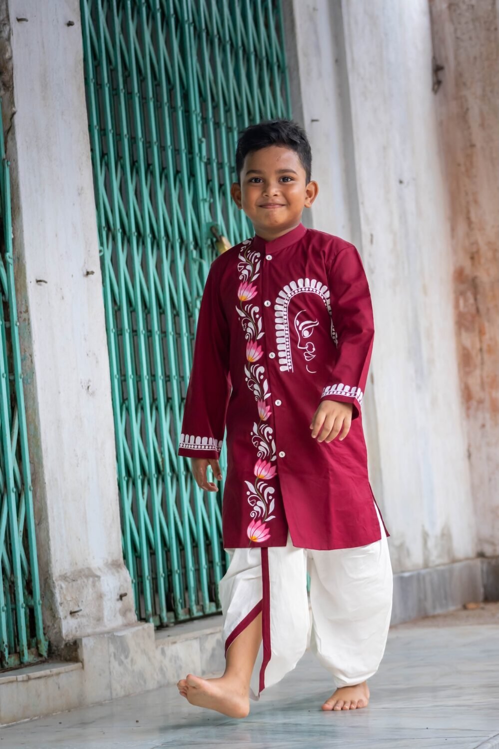 Boy walking gracefully in a maroon hand painted Bengali dhoti set designed for Durga Puja and cultural events.