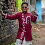 Young boy leaning against a brick wall wearing sunglasses and the Agamani maroon hand painted dhoti kurta set.