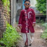 Boy walking down an outdoor alley in the Agamani hand painted maroon kurta and off-white dhoti set by Aankibukis Couture.