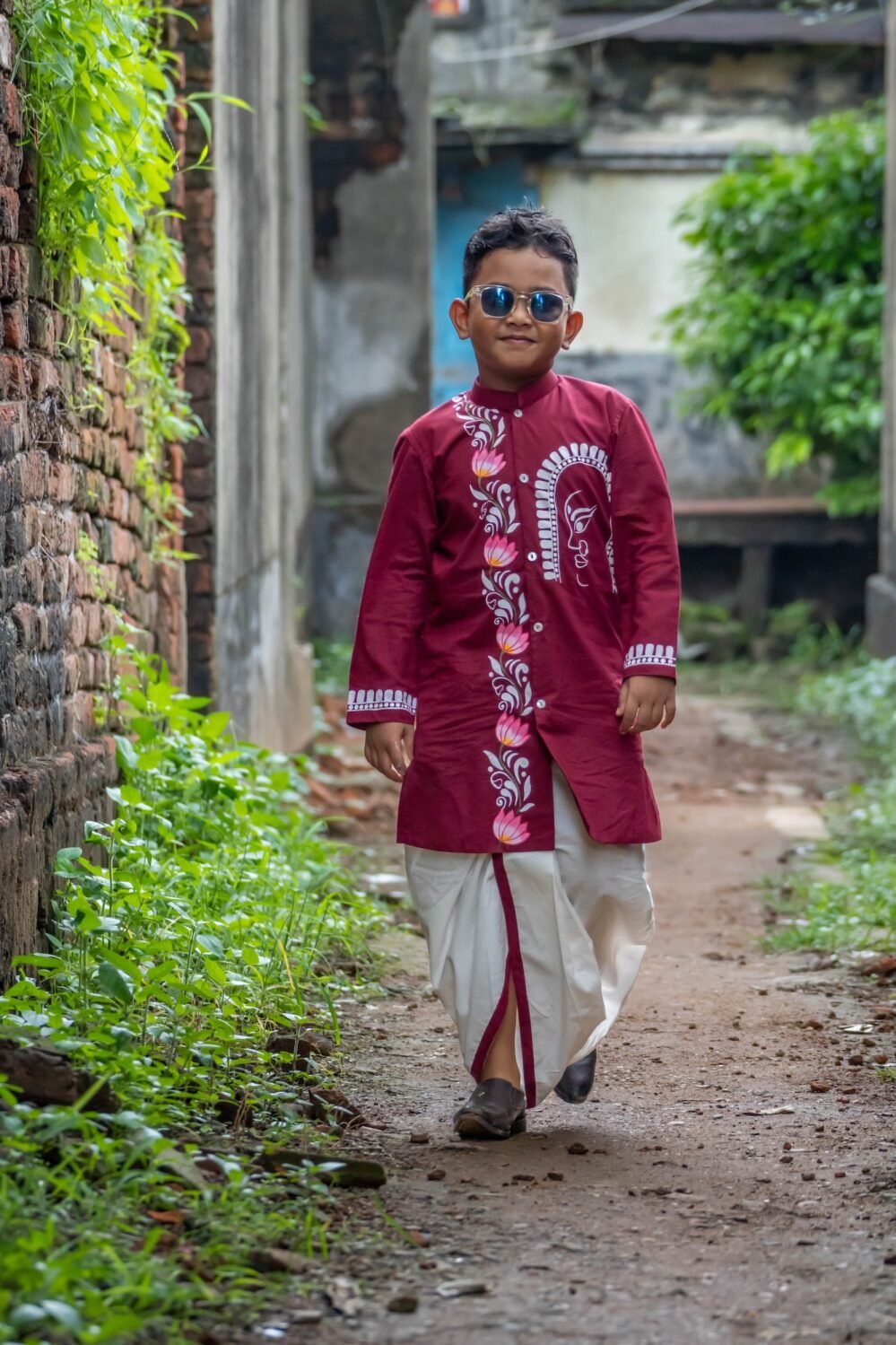 Boy walking down an outdoor alley in the Agamani hand painted maroon kurta and off-white dhoti set by Aankibukis Couture.