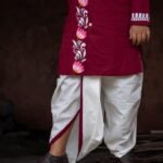 Close-up of the lower half of the Agamani maroon kurta showing the lotus vine border and off-white dhoti with maroon trim.