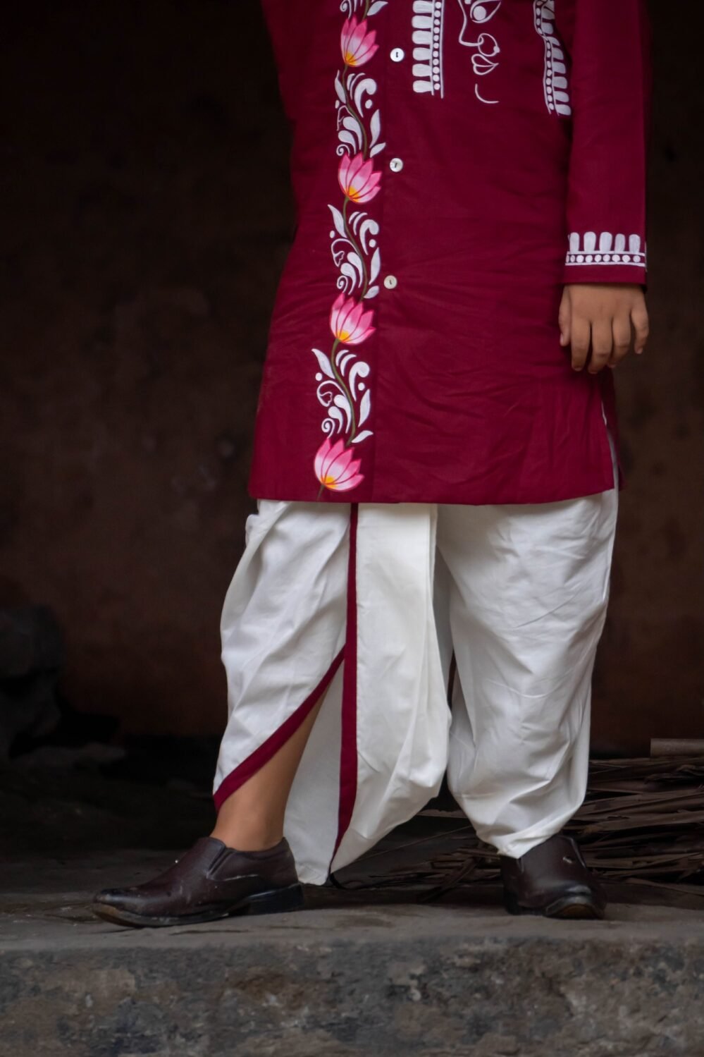 Close-up of the lower half of the Agamani maroon kurta showing the lotus vine border and off-white dhoti with maroon trim.