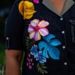 Detailed shot of hand-painted yellow, pink, and blue floral artwork on a black handloom cotton top with contrast pocket stitching.