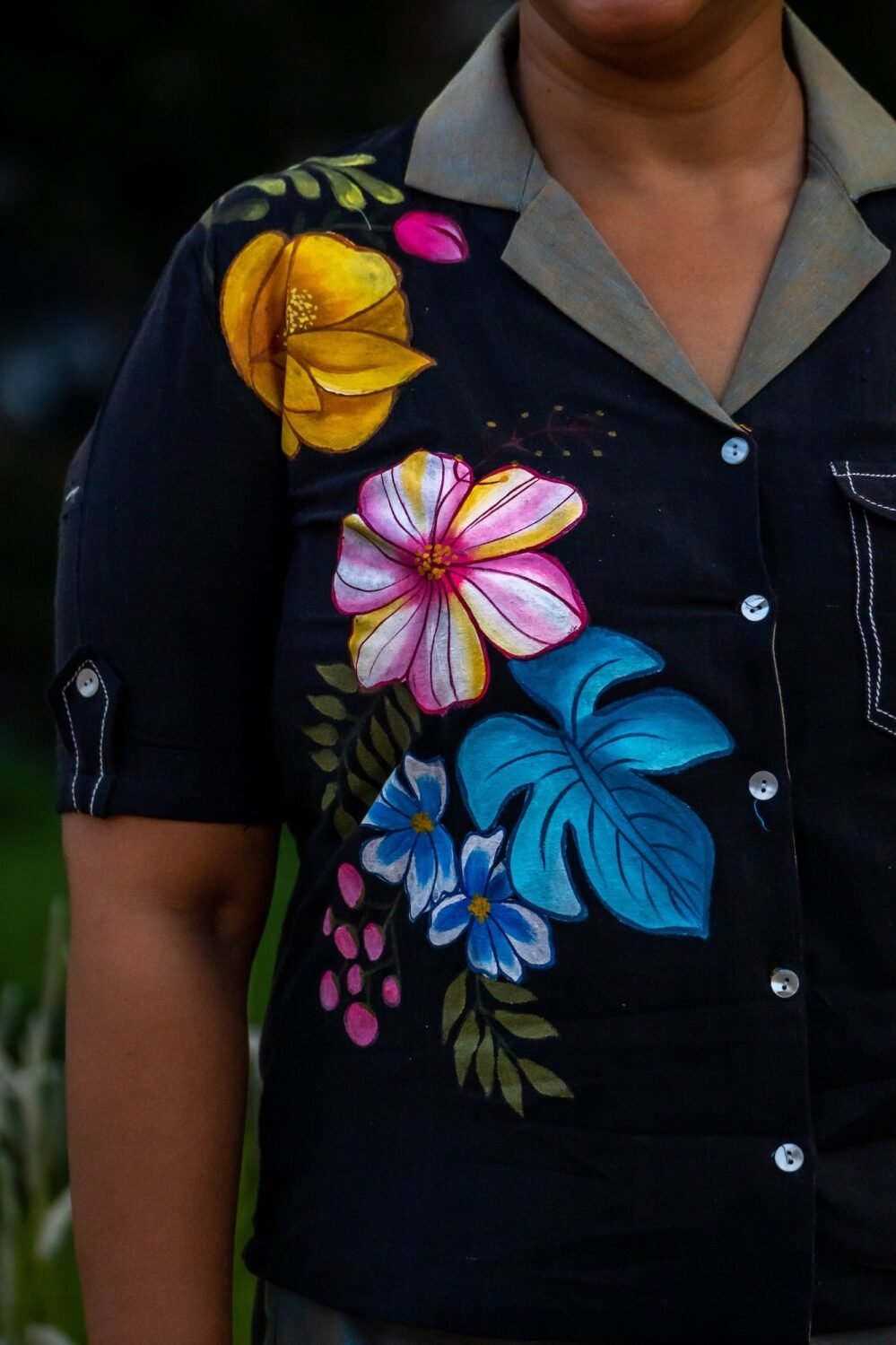 Detailed shot of hand-painted yellow, pink, and blue floral artwork on a black handloom cotton top with contrast pocket stitching.