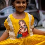 Close-up of handpainted Maa Durga and child art on the bodice of the yellow Durga Dulali frock.