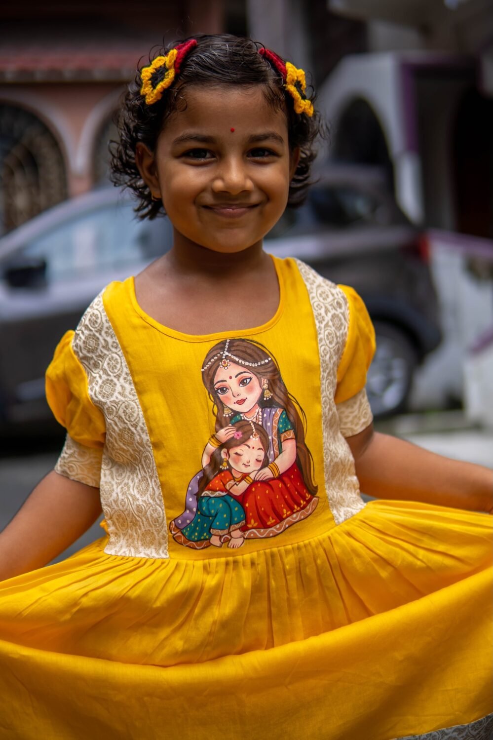 Close-up of handpainted Maa Durga and child art on the bodice of the yellow Durga Dulali frock.