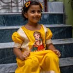 Girl sitting on marble steps wearing the handpainted Durga Dulali yellow cotton frock by Aankibukis Couture.