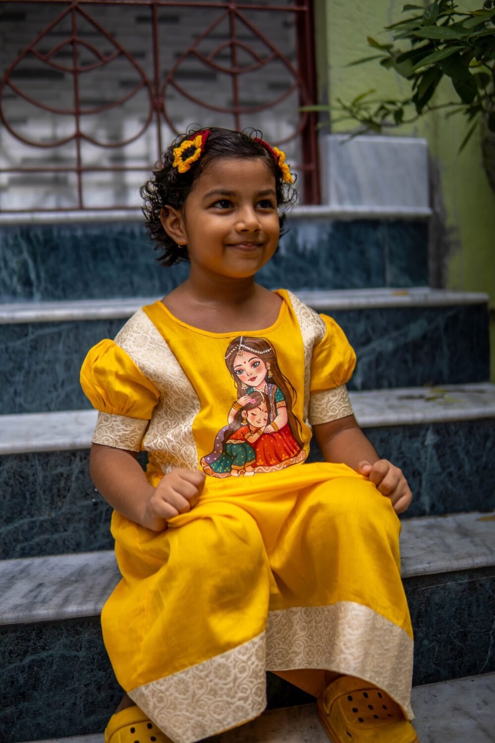 Girl sitting on marble steps wearing the handpainted Durga Dulali yellow cotton frock by Aankibukis Couture.