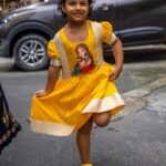 Young girl striking a playful one-legged pose wearing the yellow handpainted Durga Dulali frock with brocade border.