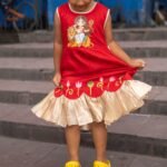 Girl looking down at her red handpainted Maa Durga frock skirt with lotus hem details.