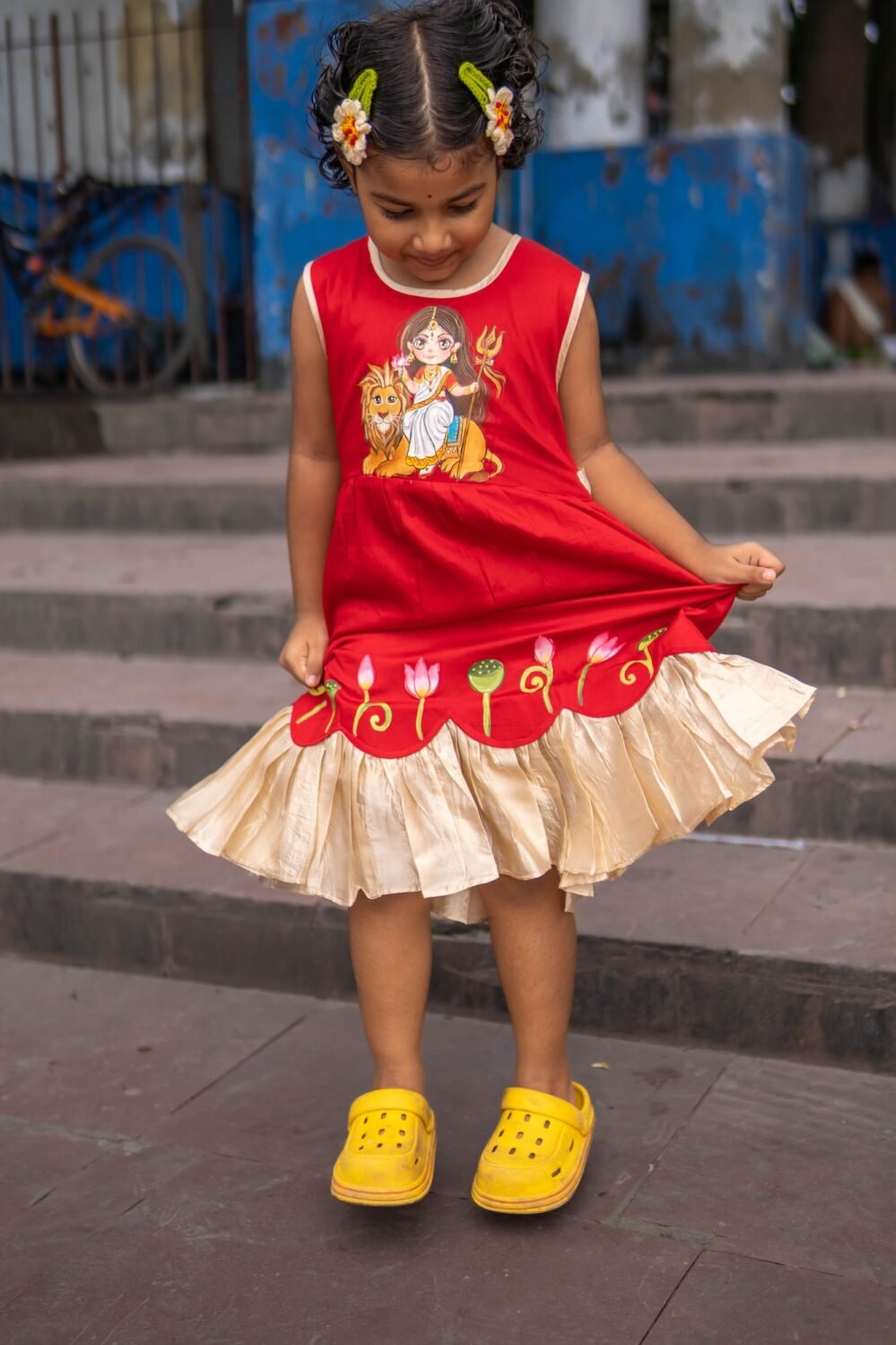 Girl looking down at her red handpainted Maa Durga frock skirt with lotus hem details.