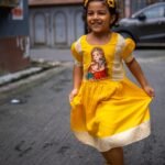 Young girl smiling and holding out her yellow handpainted Durga Dulali frock during festive celebrations.