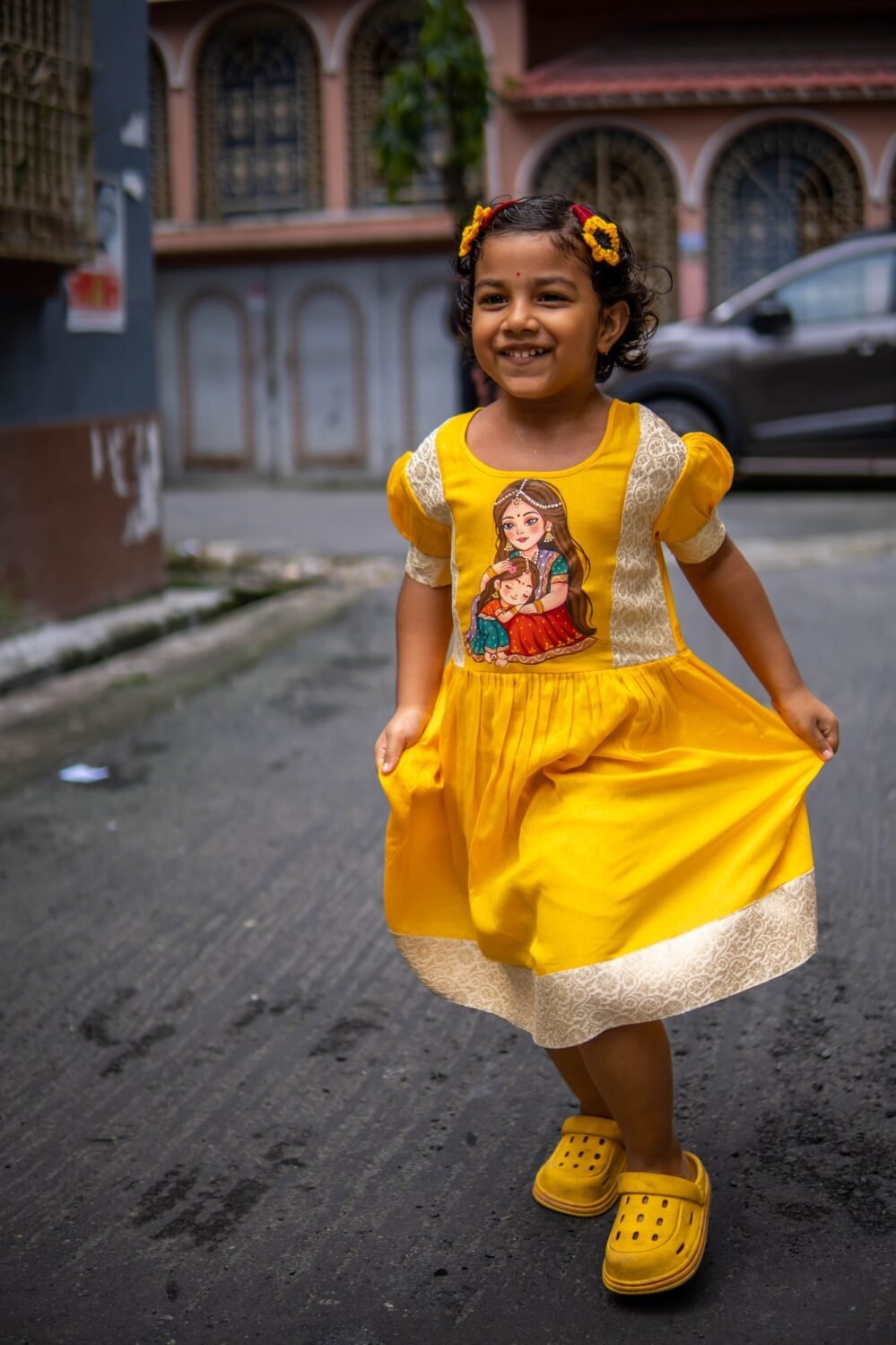 Young girl smiling and holding out her yellow handpainted Durga Dulali frock during festive celebrations.