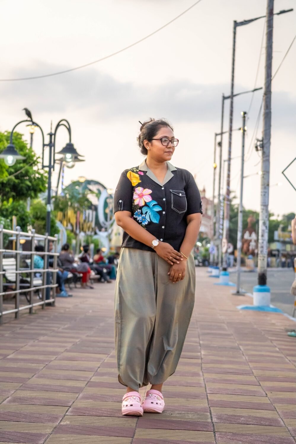 Woman posing near a park bench wearing a black blazer-collar top with hand-painted tropical flowers and beige-grey urban dhoti pants.