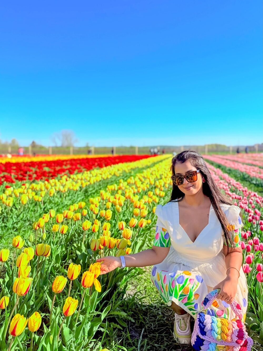 Woman holding a yellow tulip in a field, highlighting the deep neck and printed sleeve details of the off-white Tulip Dress