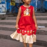 Smiling girl swaying in red malai cotton ethnic frock with golden frill hemline.