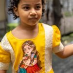 Detailed close-up view of the central handpainted Durga art and brocade trim on the kids yellow frock.