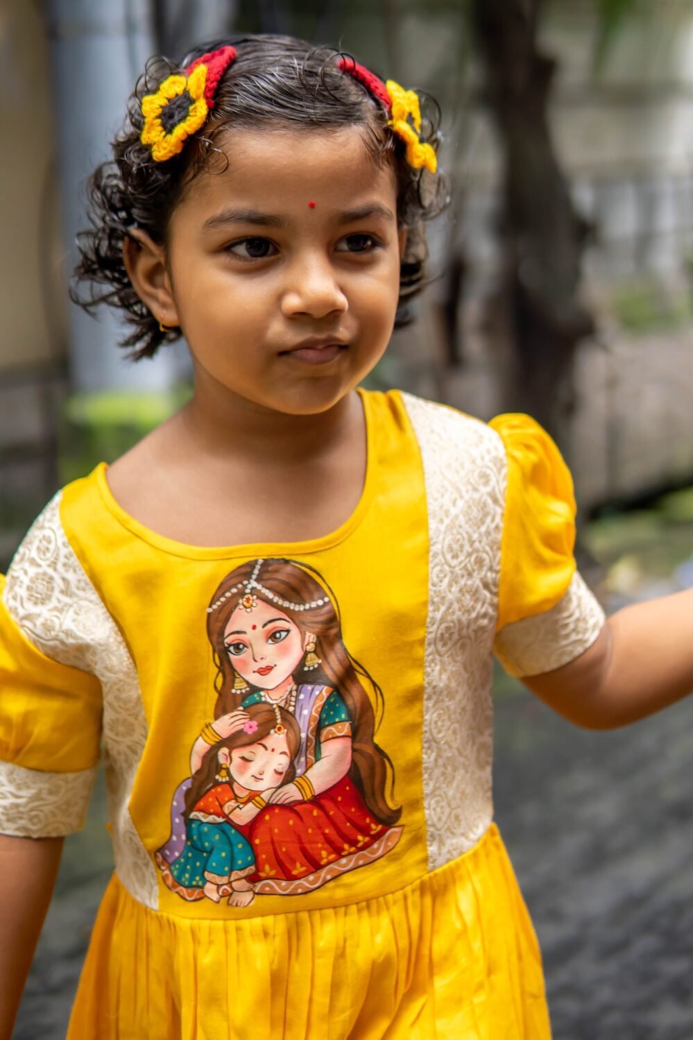 Detailed close-up view of the central handpainted Durga art and brocade trim on the kids yellow frock.