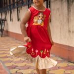 Young girl twirling in red malai cotton handpainted Maa Durga frock with golden frills.