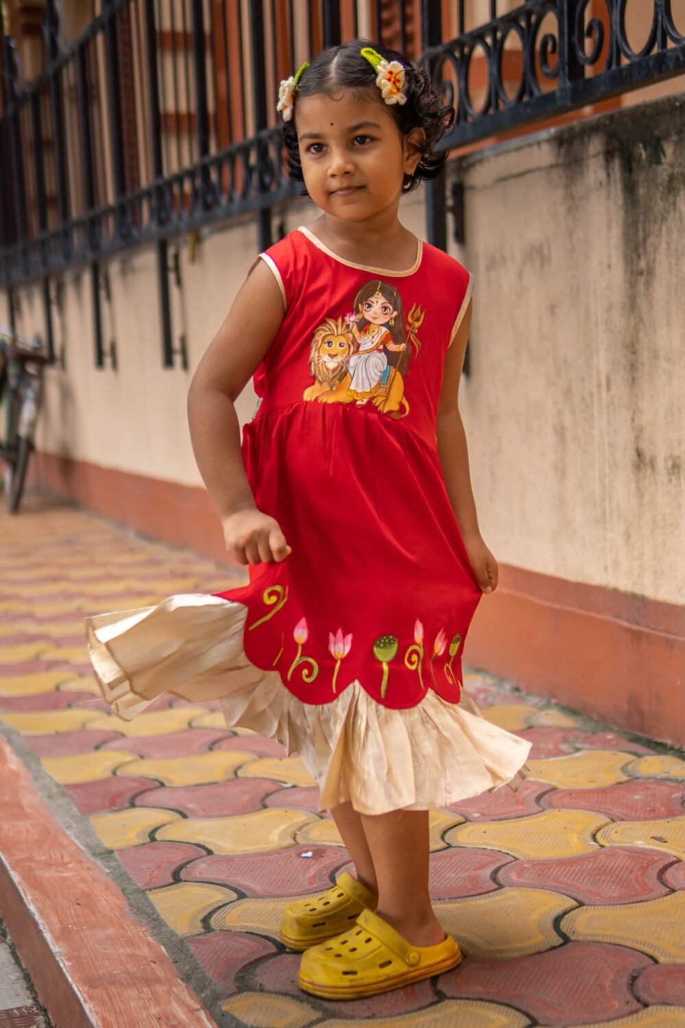 Young girl twirling in red malai cotton handpainted Maa Durga frock with golden frills.