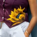 Close-up detail of the handpainted yellow sunflower motif on a purple Malai cotton waist coat hem.