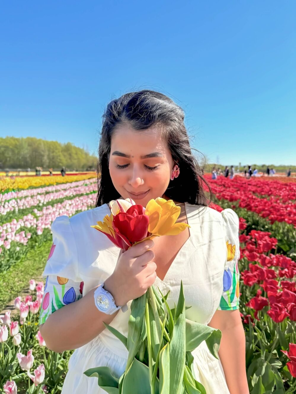 Close-up shot of a woman in a deep-neck off-white cotton dress holding a bouquet of fresh yellow and red tulips