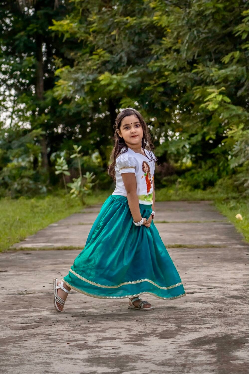 Side profile of a girl twirling in a hand-painted Maa Durga white puff-sleeve top and peacock green chiffon skirt.