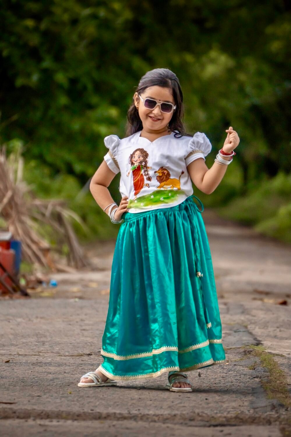 Little girl wearing sunglasses posing in Aankibukis Couture Kanya Durga skirt set with hand-painted Maa Durga top and peacock green skirt