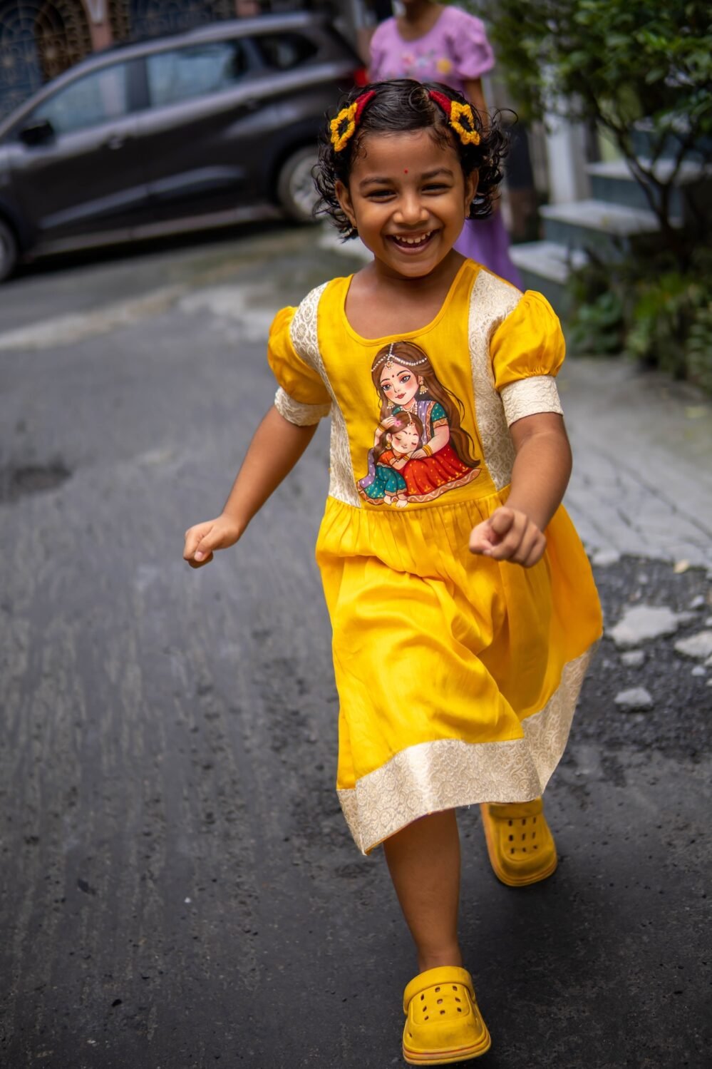 Smiling child running in the handpainted Durga Dulali yellow festive cotton frock by Aankibukis Couture.