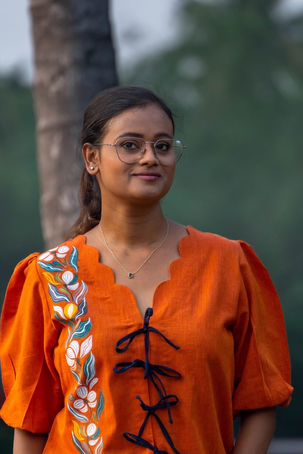Close-up portrait of woman wearing orange handpainted doori top with floral motif and puff sleeves.