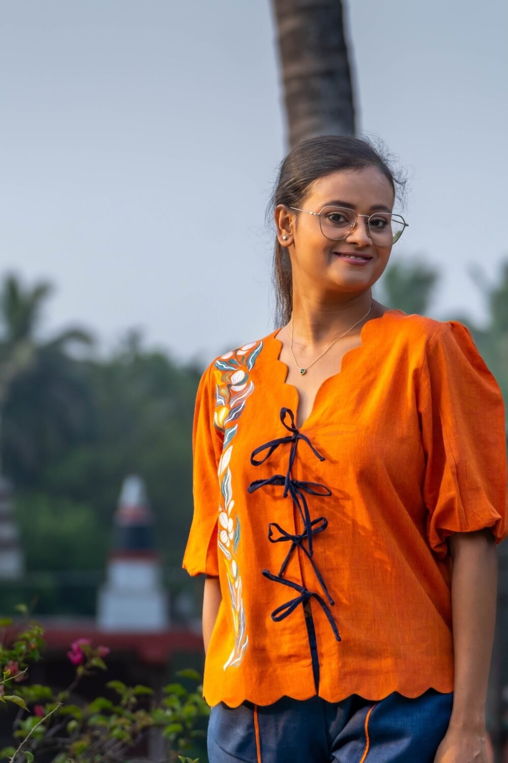 Front shot showing scalloped neck, black tie-up dooris, and handpainted florals on orange LAVA shirt.