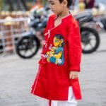 Side profile view of young boy wearing red and off white hand painted cotton dhoti kurta set for Durga Puja festival