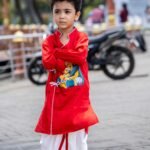 Front pose of boy wearing red cotton hand painted Maa Durga Ganesha angrakha kurta set with white piping and side ties